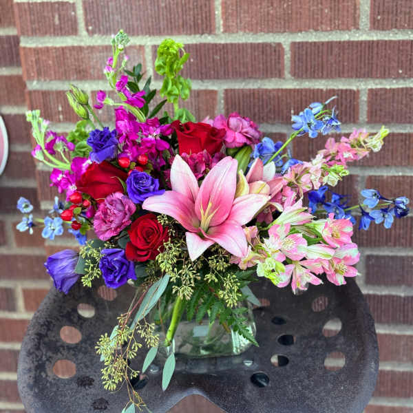 Mixed bouquet with pink lilies, red roses, and blue flowers in a glass vase