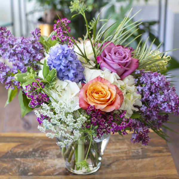 Mixed bouquet of roses, hydrangea, and purple blossoms in a clear glass vase