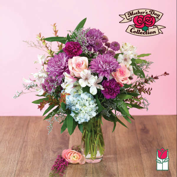 Mixed bouquet of purple mums, pink roses, and blue hydrangea in a clear glass vase