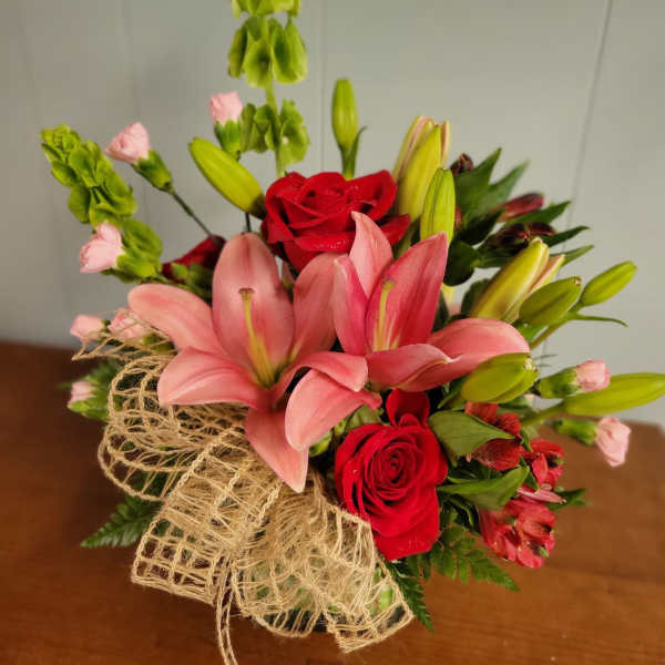 Bouquet of pink lilies and red roses with green filler in burlap wrap