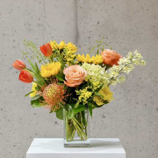 Mixed bouquet in a clear glass vase with orange, yellow, and peach flowers