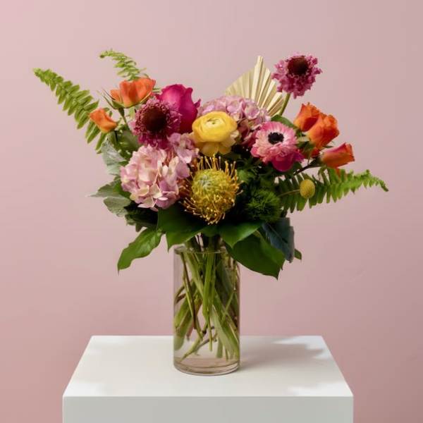 Mixed bouquet of pink, orange, and yellow flowers in a clear glass vase