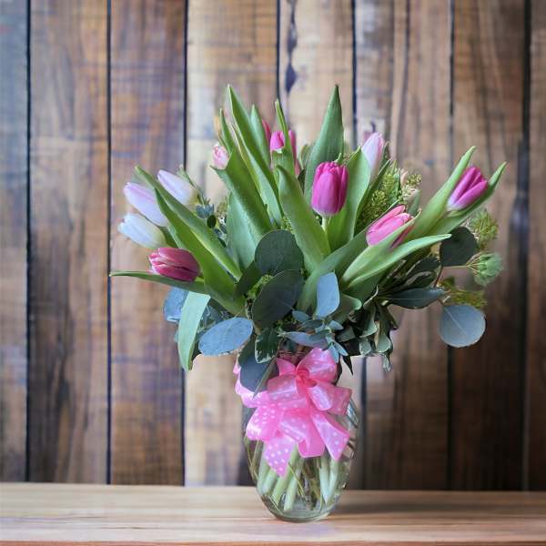 Pink and white tulips in a glass vase with a pink ribbon