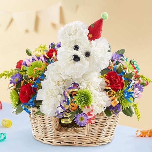 White teddy bear in a basket surrounded by colorful flowers and ribbons