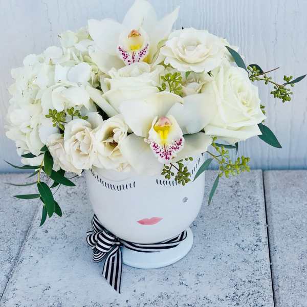 White floral arrangement in a face-shaped vase with a striped ribbon
