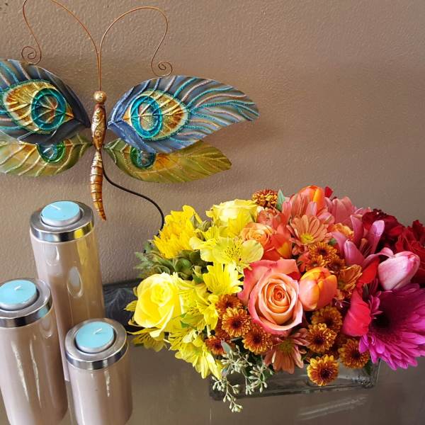Mixed bouquet in a glass vase beside three candles and a decorative butterfly wall piece