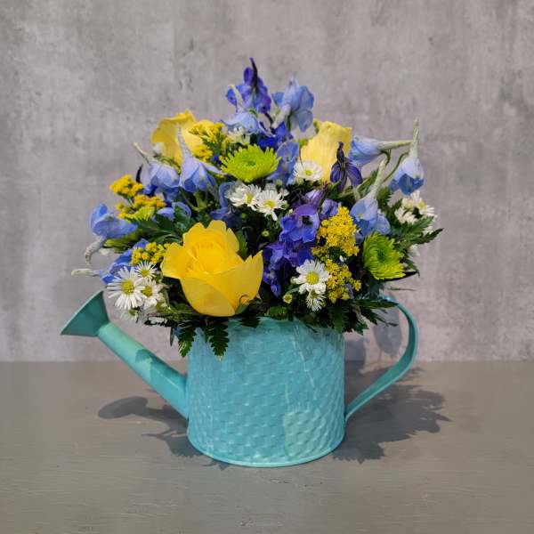Mixed bouquet in a turquoise watering can vase with yellow and blue flowers
