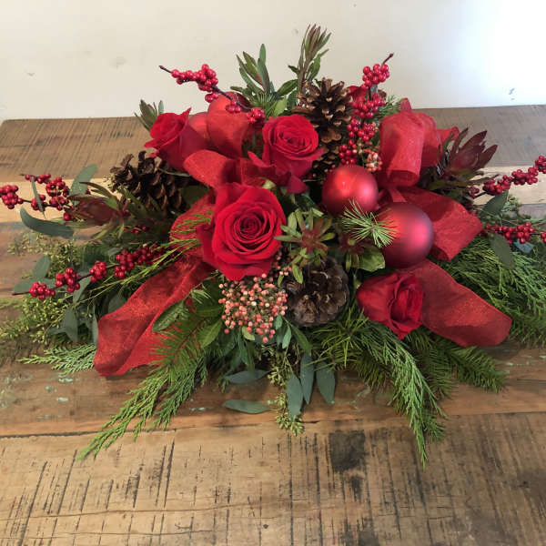 Red roses with pinecones, berries, and ribbon in a low holiday arrangement