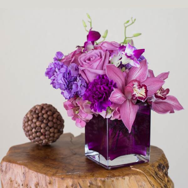 Purple floral arrangement in a square glass vase with a decorative orb beside it