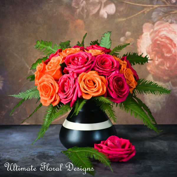Pink and orange roses arranged in a black vase with fern foliage