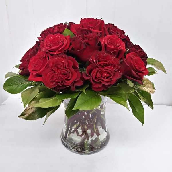 Red roses arranged in a clear glass vase with green leaves