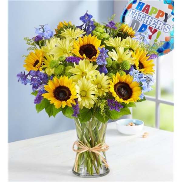 Bouquet of sunflowers, daisies, and purple flowers in a glass vase