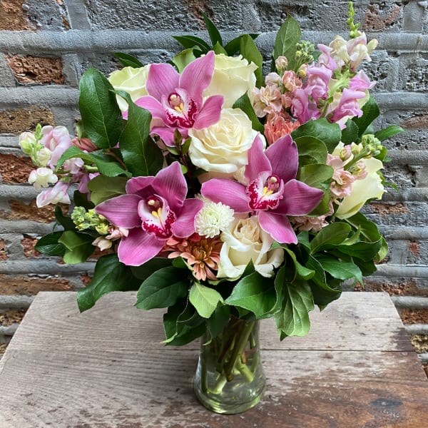 Vase arrangement of pink orchids, white roses, and pastel blooms in a clear glass cylinder