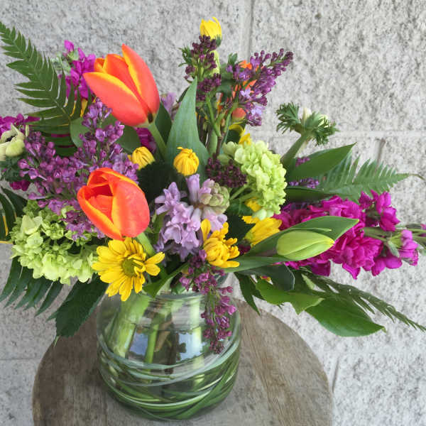 Colorful mixed bouquet in a glass vase with tulips, daisies, and purple blooms