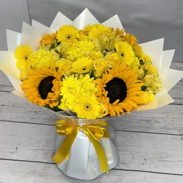 Yellow bouquet with sunflowers and mixed blooms wrapped in white paper