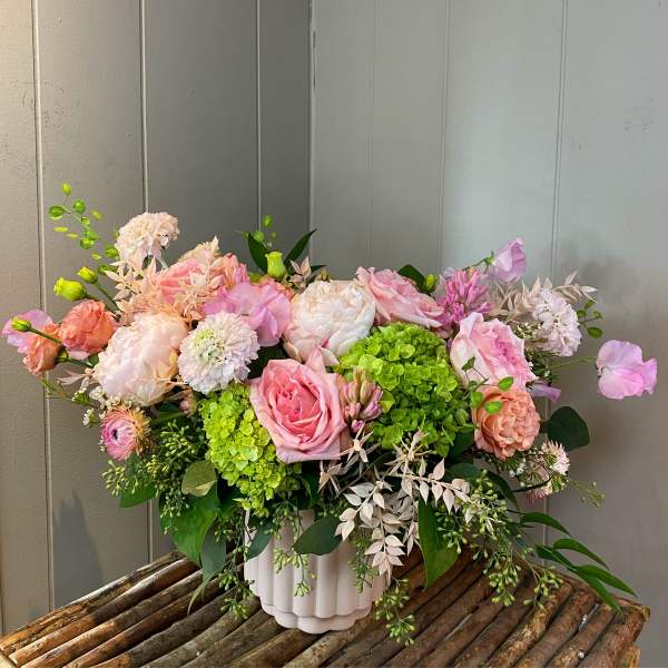 Low arrangement of pink and peach blooms with green hydrangeas in a white ceramic pot