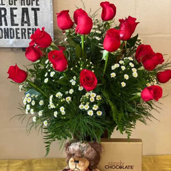 Red roses arranged with small white daisies, a teddy bear, and a chocolate box