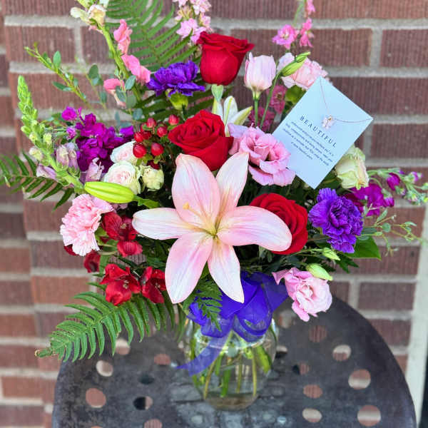 Mixed bouquet with red roses, pink lilies, and purple flowers in a glass vase
