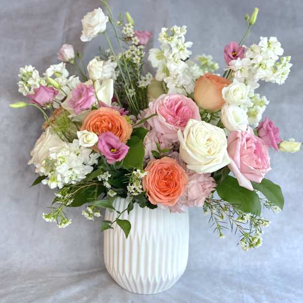 Pink, peach, and white flowers arranged in a white vase