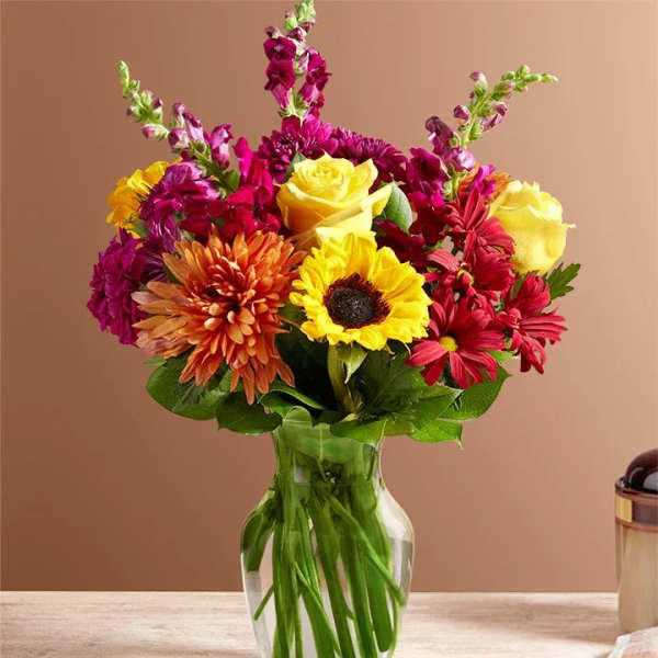 Bright mixed bouquet of sunflowers, roses, and daisies in a glass vase