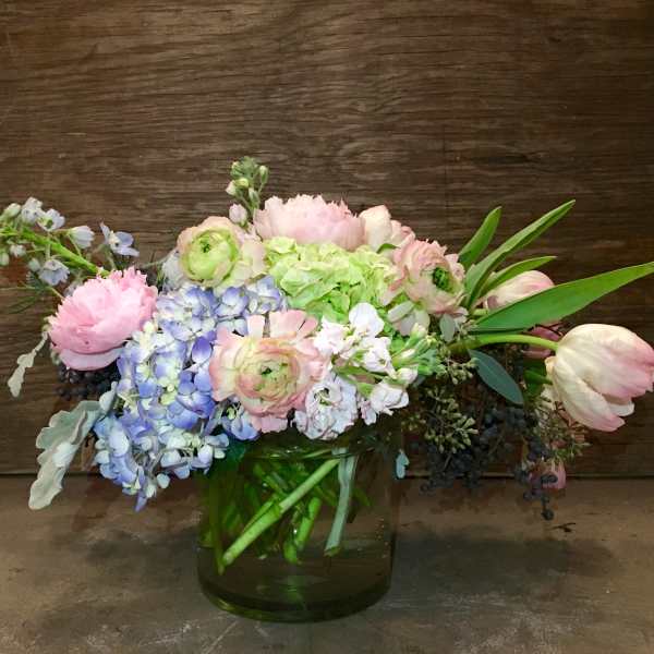 Pastel bouquet of hydrangeas, tulips, and ranunculus in a green glass vase
