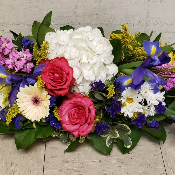 Low centerpiece of pink roses, white hydrangea, purple iris, daisies and mixed bright flowers