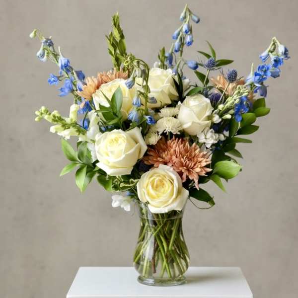 Bouquet of white roses, blue flowers, and peach blooms in a clear glass vase