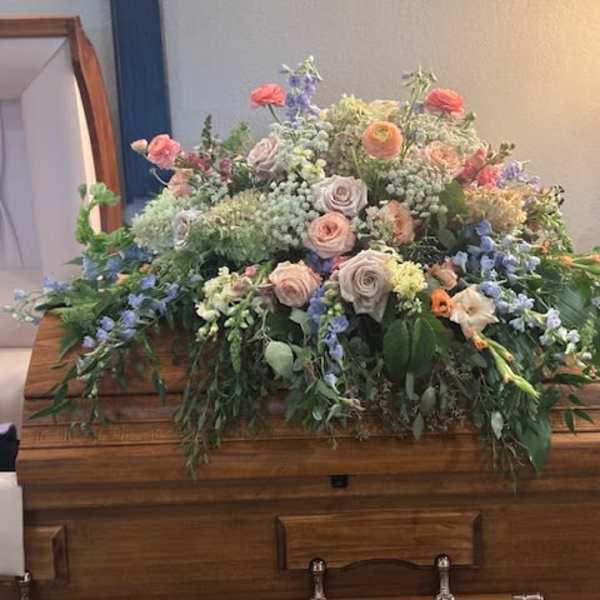 Large pastel floral arrangement on a wooden casket