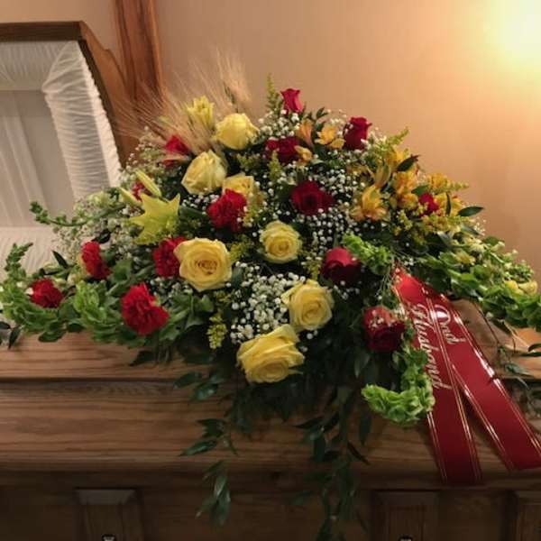 Large red and yellow floral casket spray with ribbon on a wooden casket