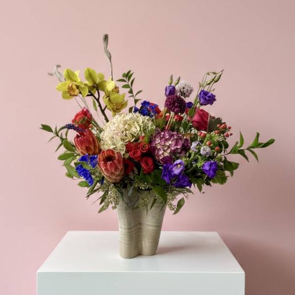 Colorful mixed flower arrangement in a beige vase on a white pedestal