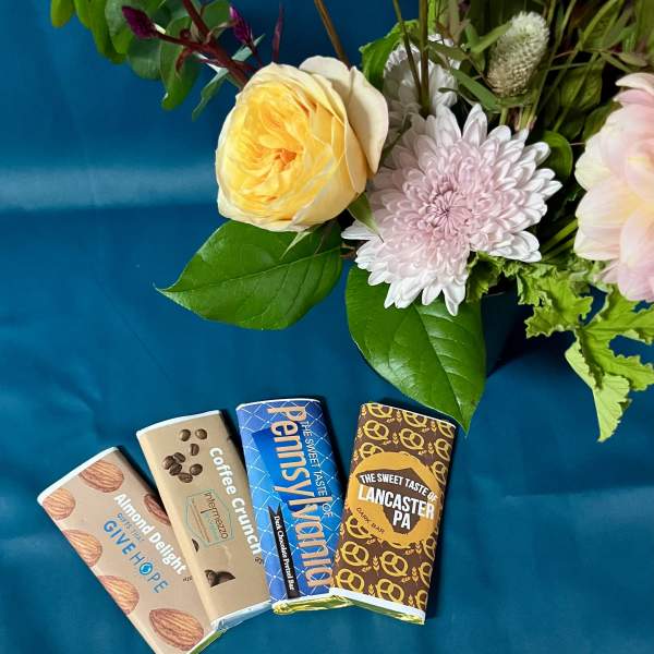 Floral arrangement with pink and yellow blooms beside four wrapped chocolate bars on teal fabric.