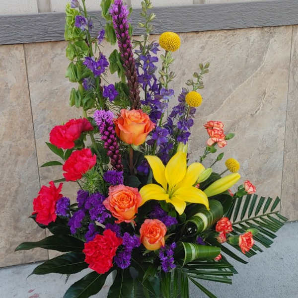 Tall mixed flower arrangement in a dark vase with yellow lilies and orange roses
