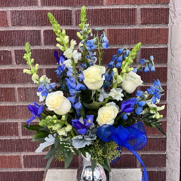 Blue and white floral arrangement in a silver vase with a blue ribbon