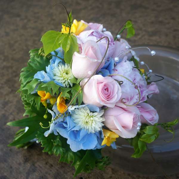 Hand-tied bouquet of pink roses, blue hydrangeas, white mums, and yellow flowers with pearl accents