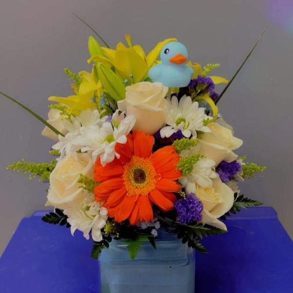 Mixed bouquet with orange gerbera, white roses, and a blue duck topper in a vase