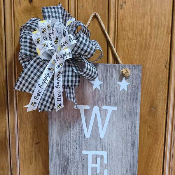 Wooden welcome sign with a black-and-white bow and bee ribbon