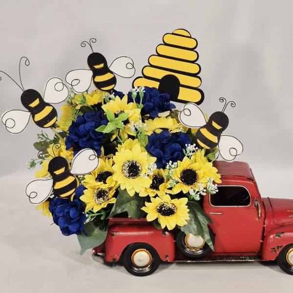 Yellow sunflowers and blue hydrangeas arranged in a red toy truck with bee decorations