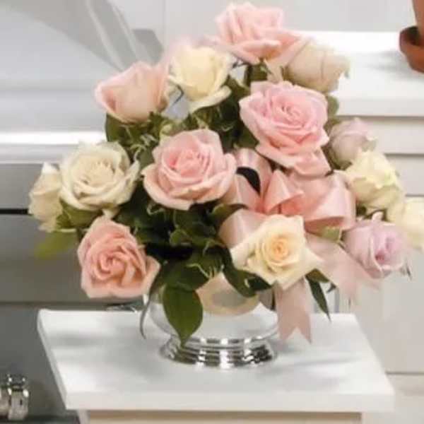 Pink and white roses arranged in a clear glass vase with a pink ribbon