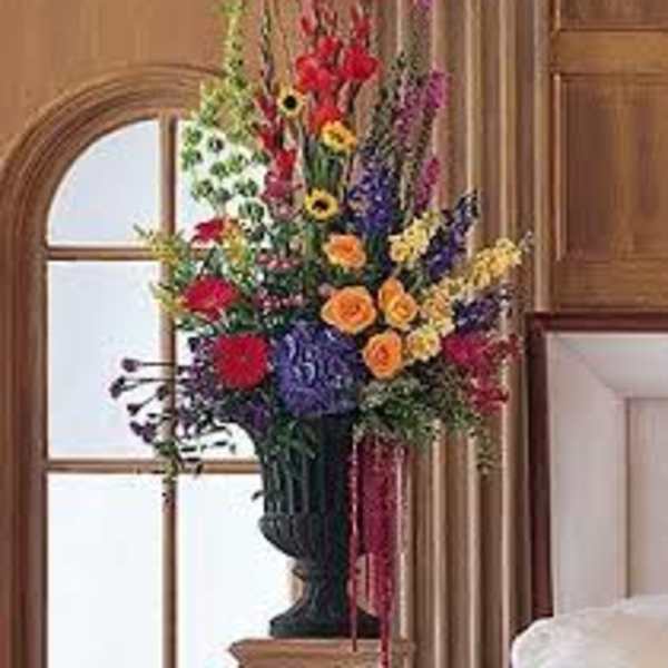Tall mixed flower arrangement in a dark vase with red, yellow, purple, and orange blooms