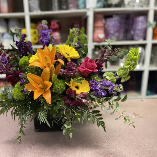 Colorful mixed flower arrangement in a black container with orange lilies and purple blooms