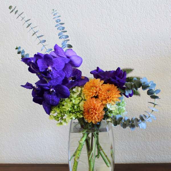 Purple orchids and orange flowers in a clear glass vase with eucalyptus