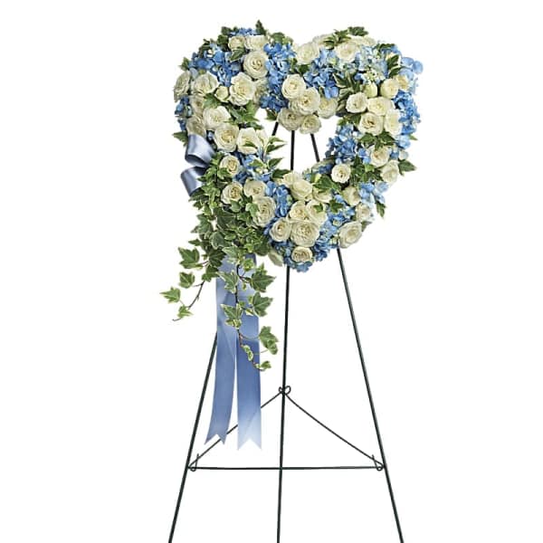 Heart-shaped blue and white floral wreath with ivy and blue ribbon on a tall easel stand.