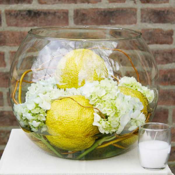White hydrangeas and yellow decorative gourds in a glass bowl