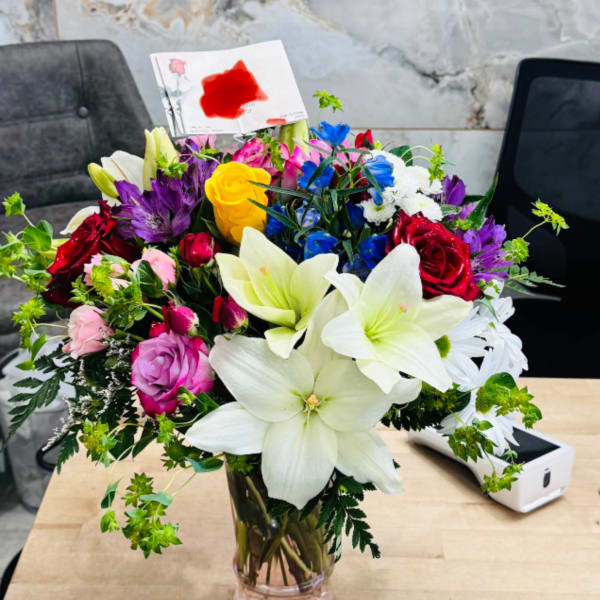 Mixed bouquet of lilies, roses, and daisies in a glass vase