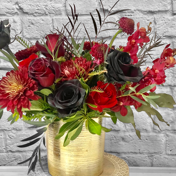 Red and black floral arrangement in a gold vase