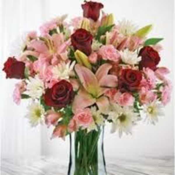 Bouquet of red roses, pink lilies, and white daisies in a glass vase