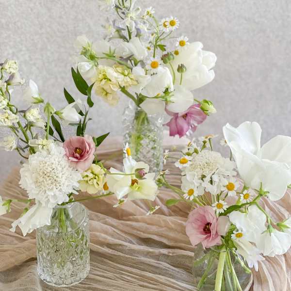 Three small floral arrangements in glass vases with white and pink blooms