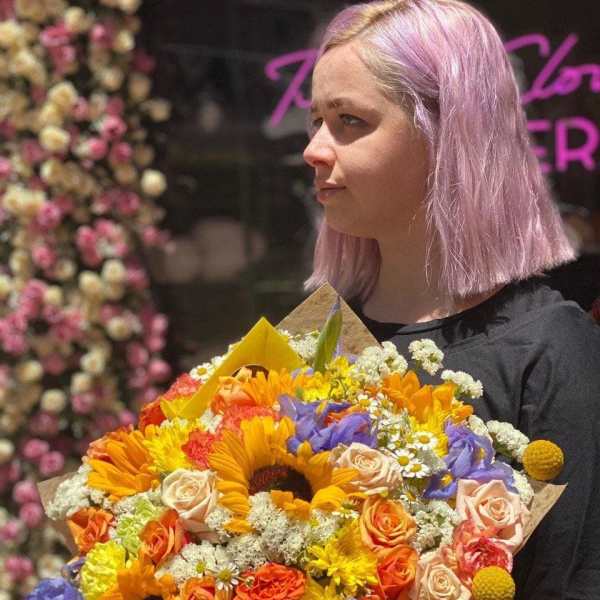 Person holding a colorful bouquet with sunflowers, roses, and purple flowers