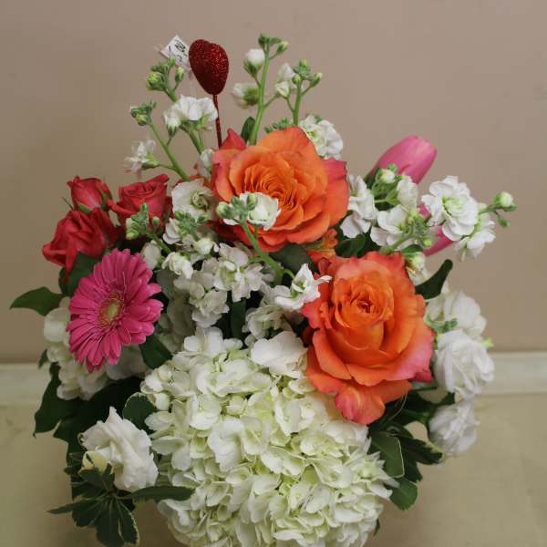 Bouquet of orange and red roses with white blooms in a red vase