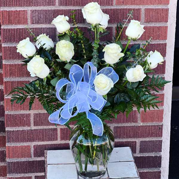 White roses arranged in a clear glass vase with a blue ribbon